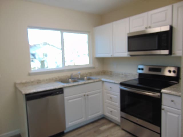 kitchen with sink, white cabinets, light hardwood / wood-style flooring, and appliances with stainless steel finishes