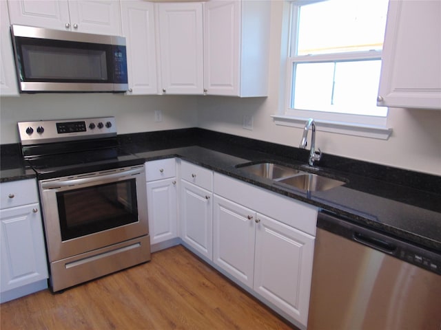 kitchen featuring light hardwood / wood-style flooring, sink, white cabinets, dark stone counters, and stainless steel appliances