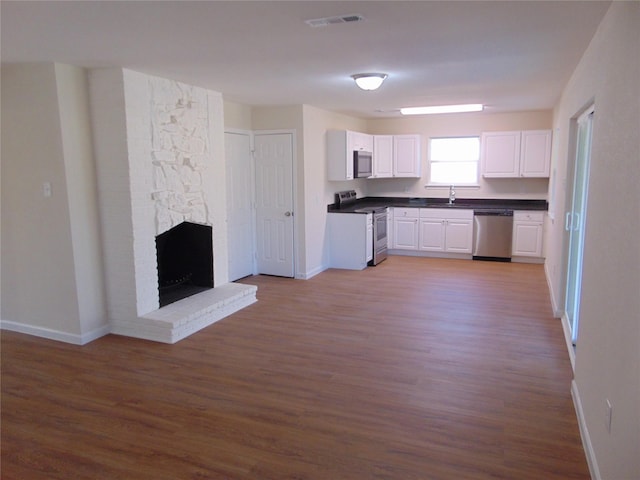 kitchen with white cabinetry, stainless steel appliances, sink, hardwood / wood-style flooring, and a brick fireplace