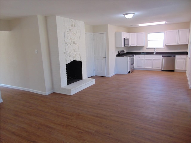 kitchen featuring white cabinets, dark hardwood / wood-style flooring, stainless steel appliances, sink, and a brick fireplace