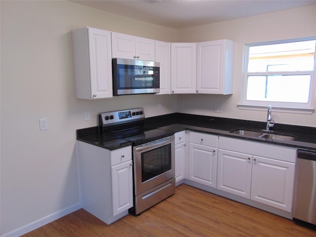 kitchen with white cabinets, appliances with stainless steel finishes, dark stone countertops, sink, and light hardwood / wood-style flooring