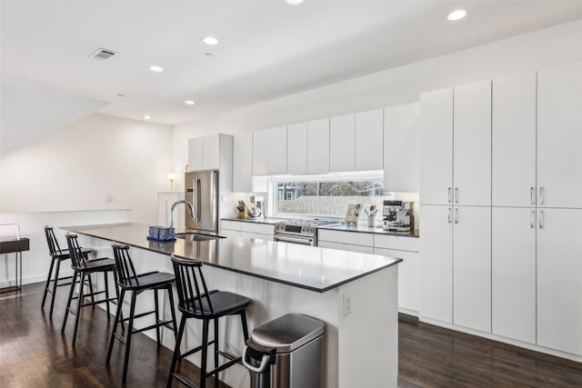 kitchen featuring dark wood-type flooring, white cabinetry, stainless steel appliances, a kitchen breakfast bar, and sink