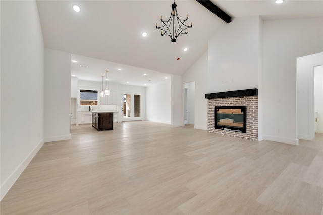 unfurnished living room featuring beam ceiling, a fireplace, high vaulted ceiling, light hardwood / wood-style floors, and an inviting chandelier