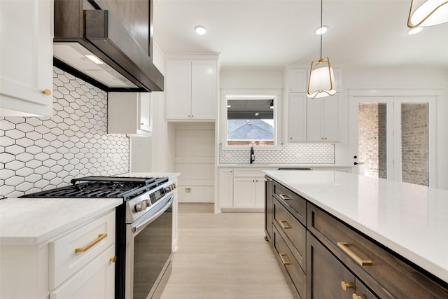 kitchen with decorative light fixtures, white cabinets, stainless steel gas range, and wall chimney exhaust hood