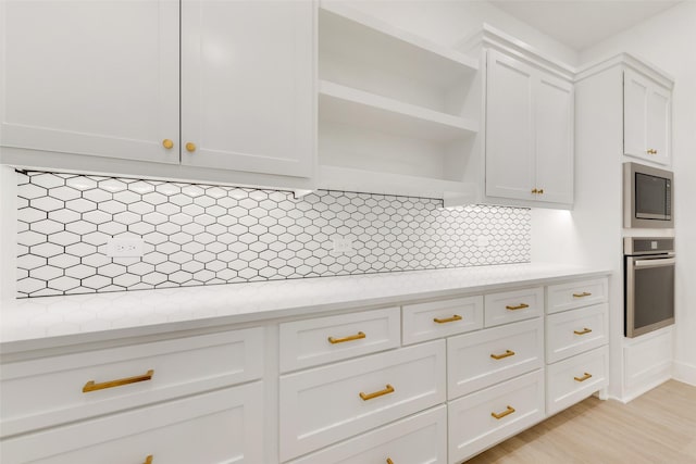 kitchen featuring light stone countertops, backsplash, white cabinets, and stainless steel appliances