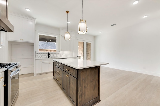 kitchen featuring pendant lighting, gas range, light wood-type flooring, white cabinetry, and a center island