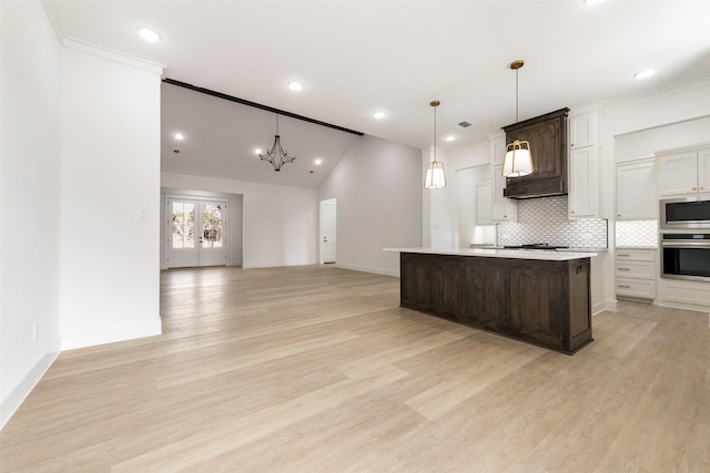 kitchen featuring appliances with stainless steel finishes, lofted ceiling, light hardwood / wood-style flooring, decorative backsplash, and a center island with sink