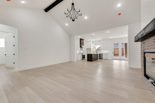 unfurnished living room with an inviting chandelier, high vaulted ceiling, a brick fireplace, light hardwood / wood-style flooring, and beam ceiling