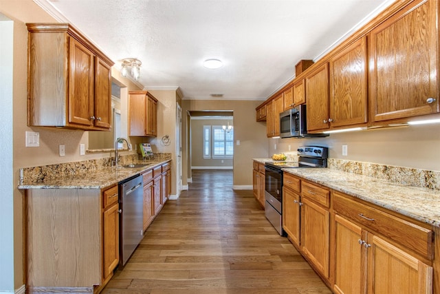 kitchen with light stone countertops, appliances with stainless steel finishes, sink, light hardwood / wood-style flooring, and ornamental molding