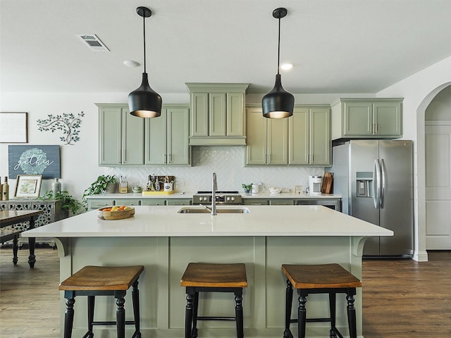 kitchen featuring decorative backsplash, pendant lighting, stainless steel fridge, and an island with sink