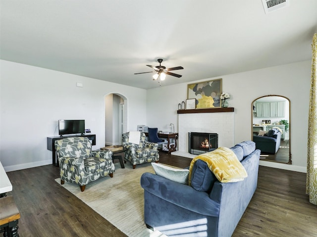 living room featuring ceiling fan, dark hardwood / wood-style floors, and a fireplace