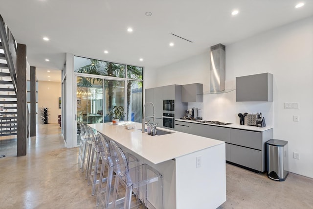 kitchen featuring a breakfast bar, wall chimney range hood, a large island with sink, and gray cabinetry