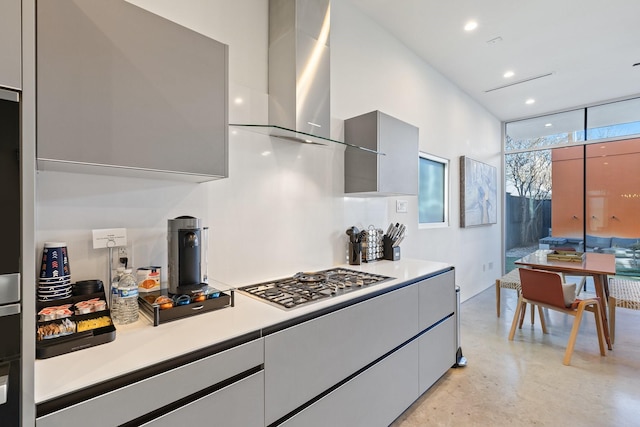 kitchen featuring a wall of windows, stainless steel gas stovetop, wall chimney range hood, and gray cabinetry