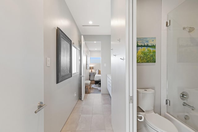 bathroom featuring a healthy amount of sunlight, bath / shower combo with glass door, tile patterned floors, and toilet