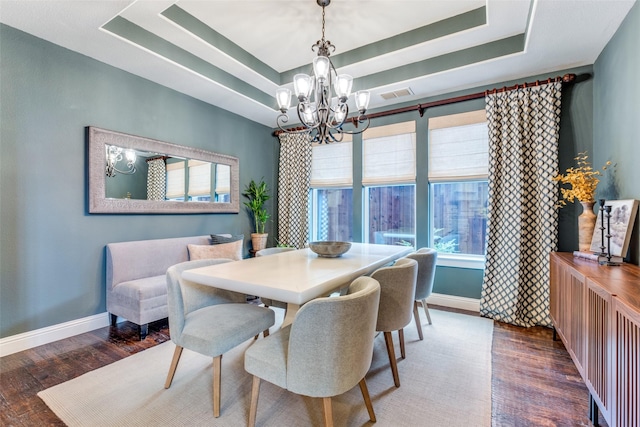 dining area with a notable chandelier, a raised ceiling, and dark hardwood / wood-style floors