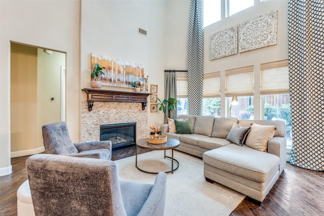 living room featuring a towering ceiling, a stone fireplace, and dark hardwood / wood-style flooring