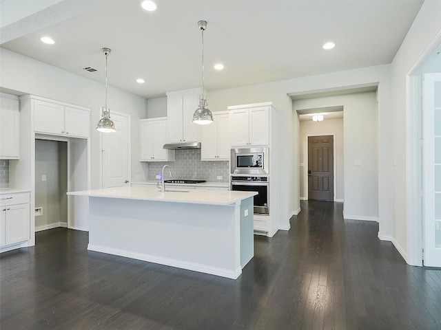 kitchen featuring appliances with stainless steel finishes, white cabinets, dark wood-type flooring, an island with sink, and decorative backsplash