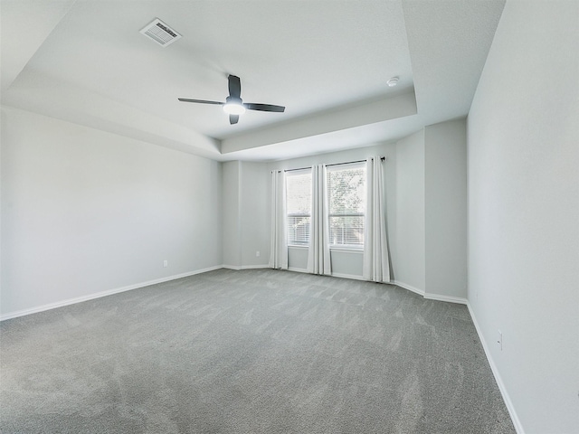 carpeted empty room with ceiling fan and a raised ceiling