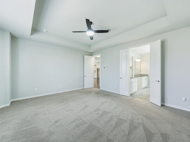 unfurnished bedroom featuring ceiling fan, ensuite bath, light carpet, and a raised ceiling