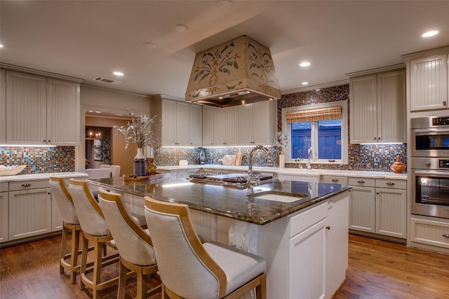 kitchen featuring a kitchen bar, a kitchen island with sink, dark stone counters, and stainless steel appliances