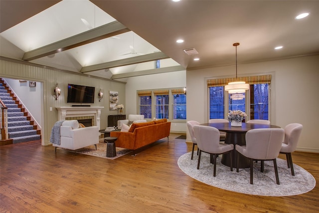 dining room featuring wood-type flooring, a tile fireplace, and vaulted ceiling with beams