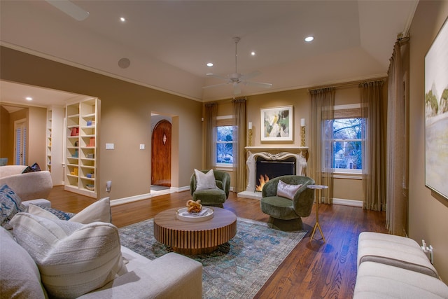 living room featuring ceiling fan, dark hardwood / wood-style flooring, crown molding, and a fireplace