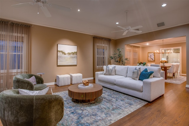 living room featuring hardwood / wood-style flooring, crown molding, and ceiling fan with notable chandelier