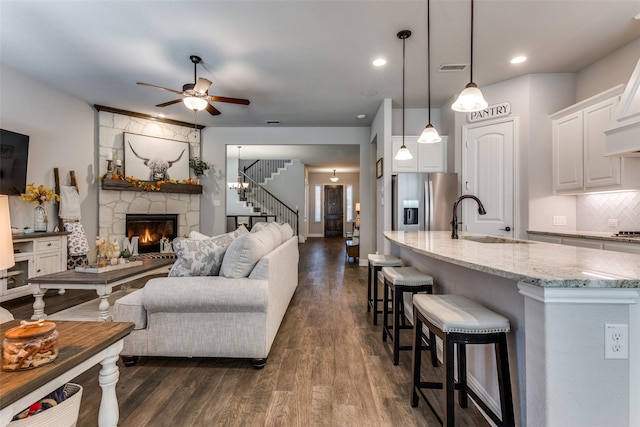 living room with sink, ceiling fan, a stone fireplace, and dark hardwood / wood-style flooring