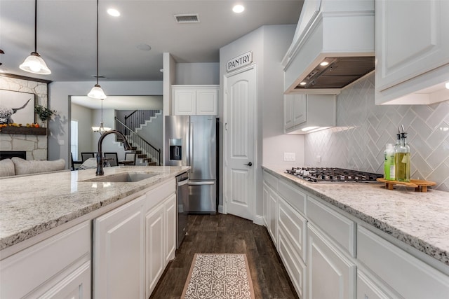 kitchen with white cabinets, appliances with stainless steel finishes, premium range hood, sink, and hanging light fixtures