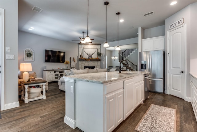 kitchen featuring light stone countertops, sink, white cabinets, decorative light fixtures, and an island with sink