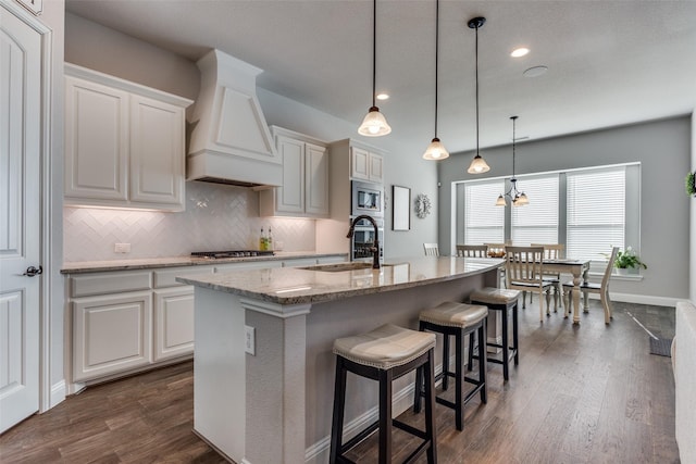 kitchen featuring backsplash, appliances with stainless steel finishes, a center island with sink, and custom range hood