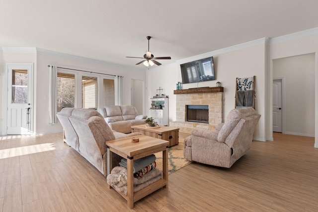 living room featuring light hardwood / wood-style floors, ceiling fan, crown molding, and a stone fireplace