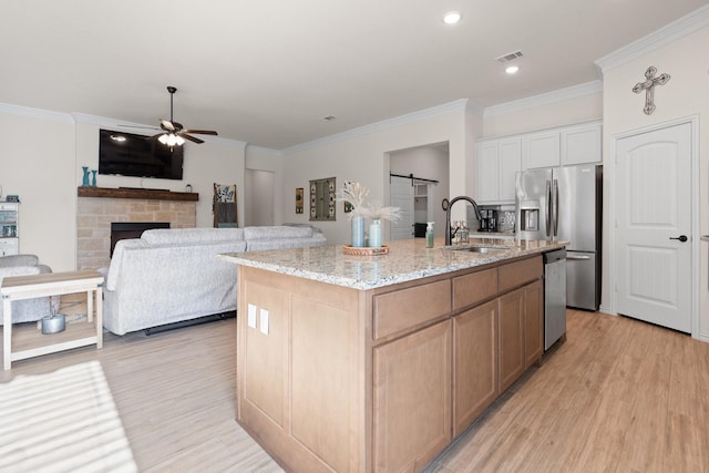 kitchen with light stone countertops, white cabinetry, sink, a kitchen island with sink, and a barn door