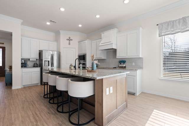 kitchen with white cabinets, stainless steel appliances, a kitchen island with sink, and decorative backsplash