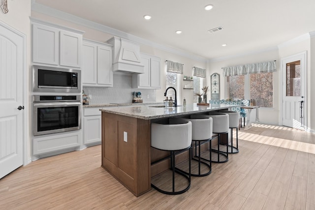 kitchen with white cabinetry, a healthy amount of sunlight, a kitchen island with sink, and appliances with stainless steel finishes