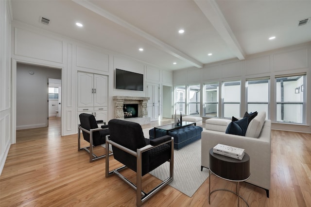 living room featuring beam ceiling, a stone fireplace, and light wood-type flooring