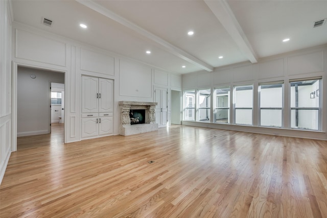 unfurnished living room featuring a fireplace, light hardwood / wood-style floors, beamed ceiling, and a healthy amount of sunlight