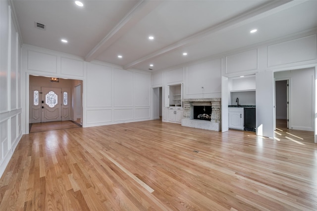 unfurnished living room featuring sink, light hardwood / wood-style floors, and beamed ceiling