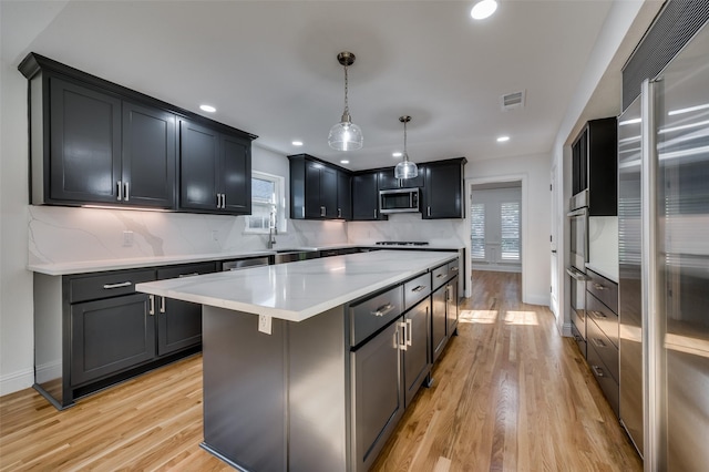 kitchen with a center island, appliances with stainless steel finishes, hanging light fixtures, decorative backsplash, and light wood-type flooring