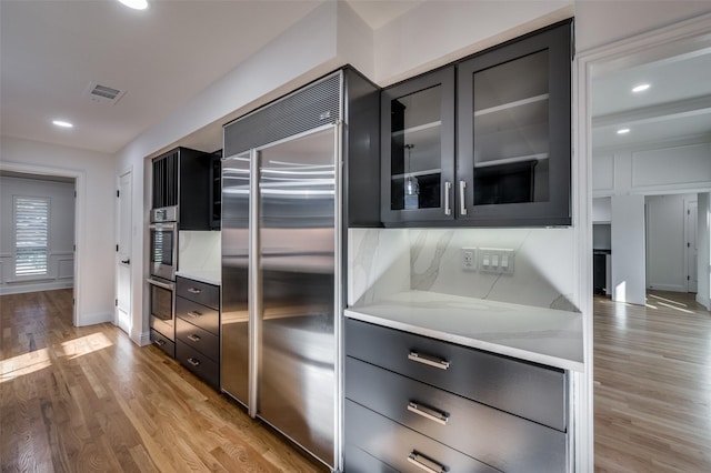 kitchen with backsplash, light wood-type flooring, light stone countertops, and stainless steel appliances