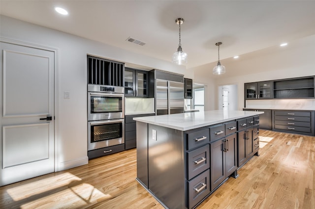 kitchen featuring a center island, light stone countertops, light hardwood / wood-style floors, appliances with stainless steel finishes, and decorative light fixtures