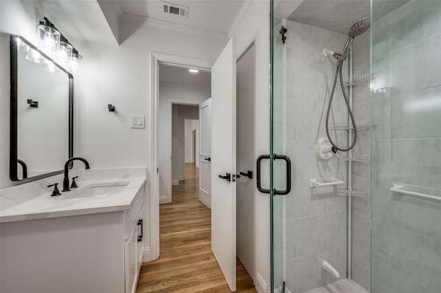 bathroom with a shower with shower door, hardwood / wood-style floors, vanity, and ornamental molding