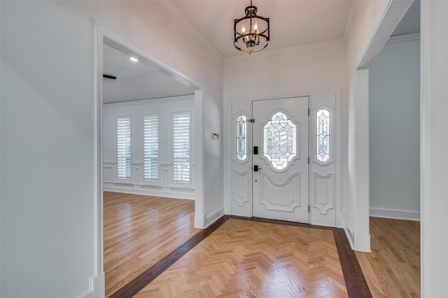 entrance foyer featuring ornamental molding, an inviting chandelier, and light parquet flooring