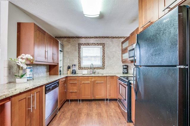 kitchen featuring sink, light wood-type flooring, backsplash, stainless steel appliances, and light stone counters