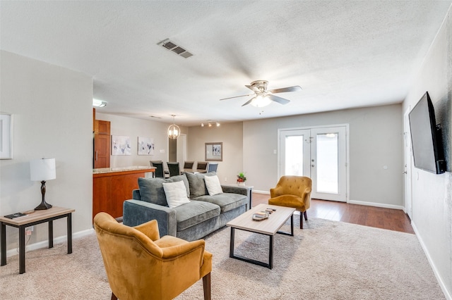 carpeted living room featuring a textured ceiling, a notable chandelier, and french doors