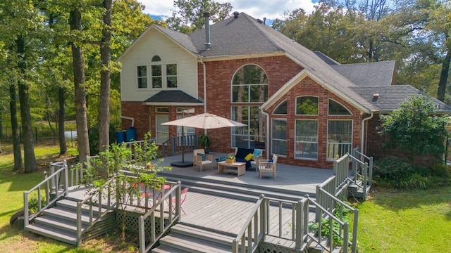 rear view of property featuring a deck, brick siding, a shingled roof, a yard, and an outdoor living space with a fire pit