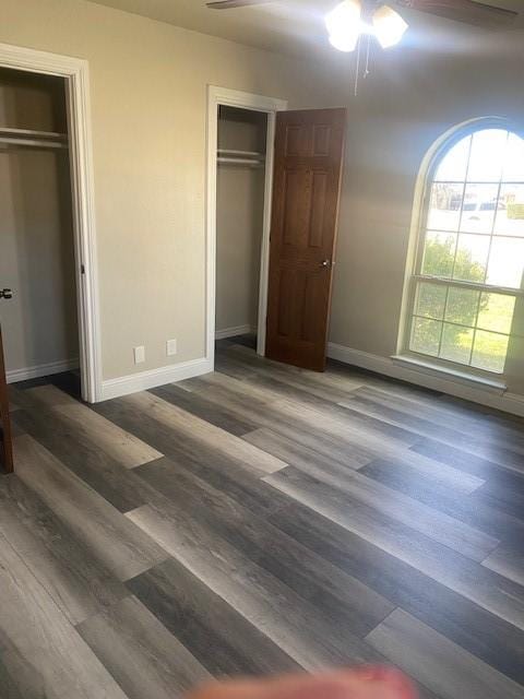 unfurnished bedroom with dark hardwood / wood-style flooring, two closets, and ceiling fan