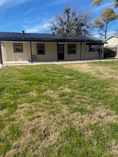 back of property with solar panels, a yard, and a patio area