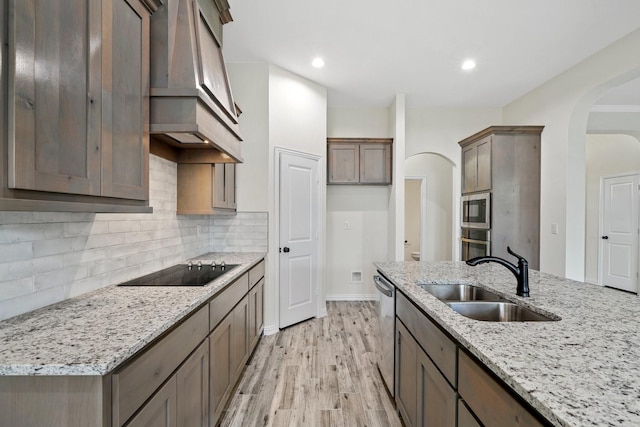 kitchen featuring appliances with stainless steel finishes, sink, custom range hood, light wood-type flooring, and light stone countertops