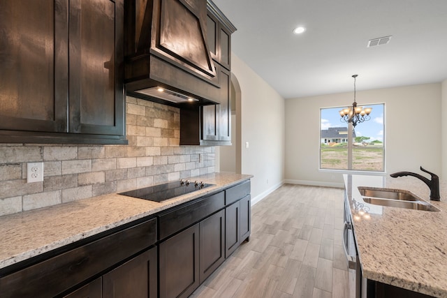 kitchen featuring light stone countertops, decorative light fixtures, sink, backsplash, and black electric cooktop